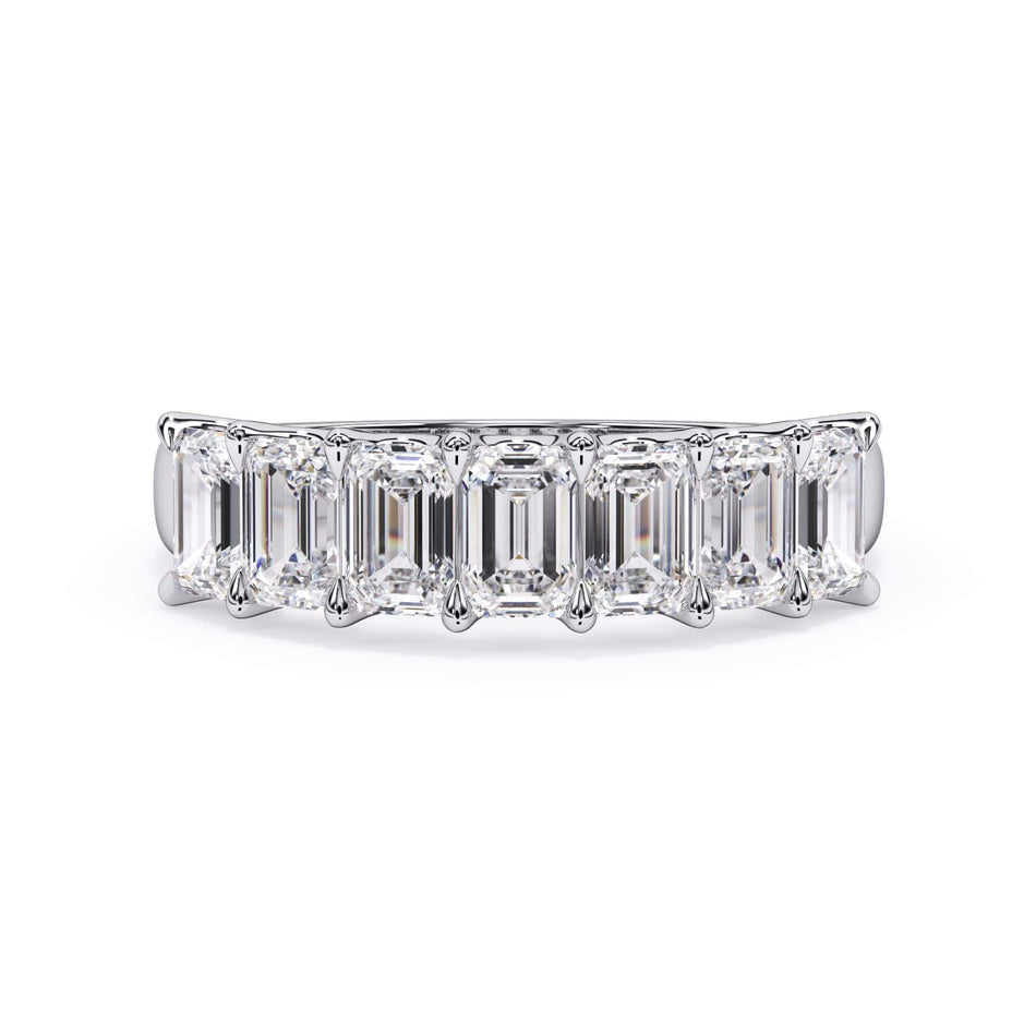 A picture of a seven stone diamond wedding ring with emerald cut diamonds that are U prong set in white gold or platinum on a white background with the ring facing forward, lying down.