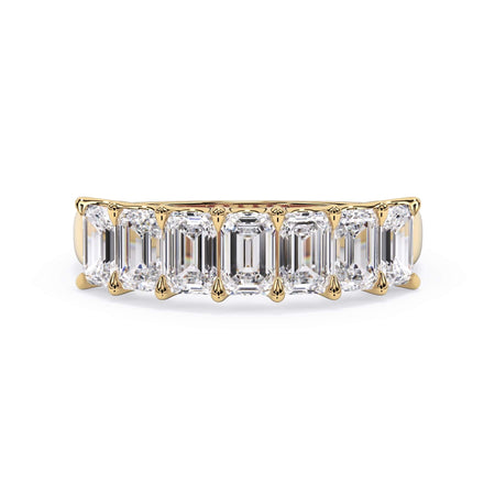 A picture of a seven stone diamond wedding ring with emerald cut diamonds that are U prong set in yellow gold on a white background with the ring facing forward, lying down.