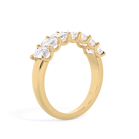 A picture of a seven stone diamond wedding ring with emerald cut diamonds that are U prong set in yellow gold on a white background with a slightly angled, through the finger view.