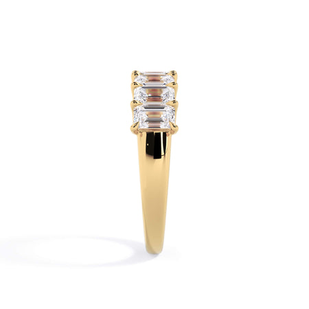 A picture of a seven stone diamond wedding ring with emerald cut diamonds that are U prong set in yellow gold on a white background with a side profile view.