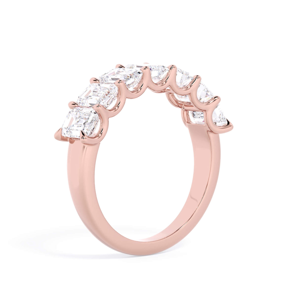 A picture of a seven stone diamond wedding ring with emerald cut diamonds that are U prong set in rose gold on a white background with a slightly angled, through the finger view.