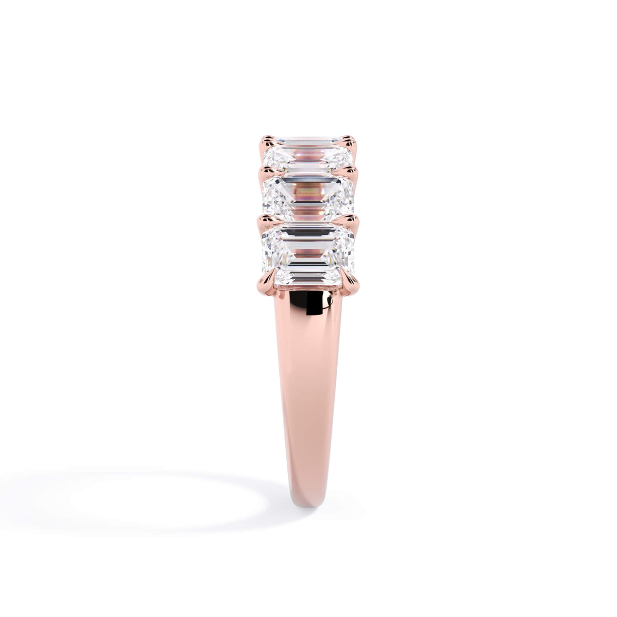 A picture of a seven stone diamond wedding ring with emerald cut diamonds that are U prong set in rose gold on a white background with a side profile view.
