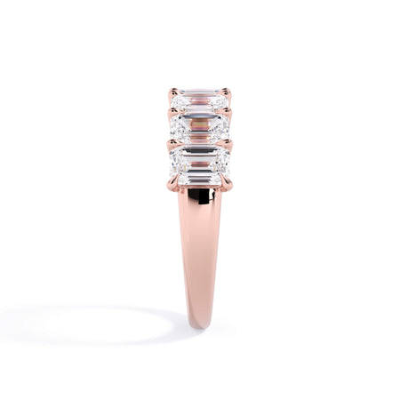 A picture of a seven stone diamond wedding ring with emerald cut diamonds that are U prong set in rose gold on a white background with a side profile view.