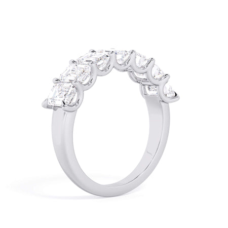 A picture of a seven stone diamond wedding ring with emerald cut diamonds that are U prong set in white gold or platinum on a white background with a slightly angled, through the finger view.