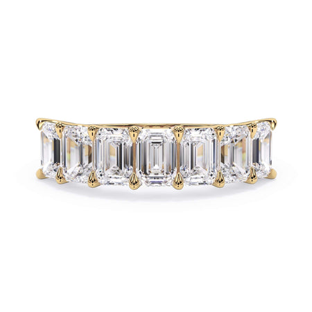 A picture of a seven stone diamond wedding ring with emerald cut diamonds that are U prong set in yellow gold on a white background with the ring facing forward, lying down.