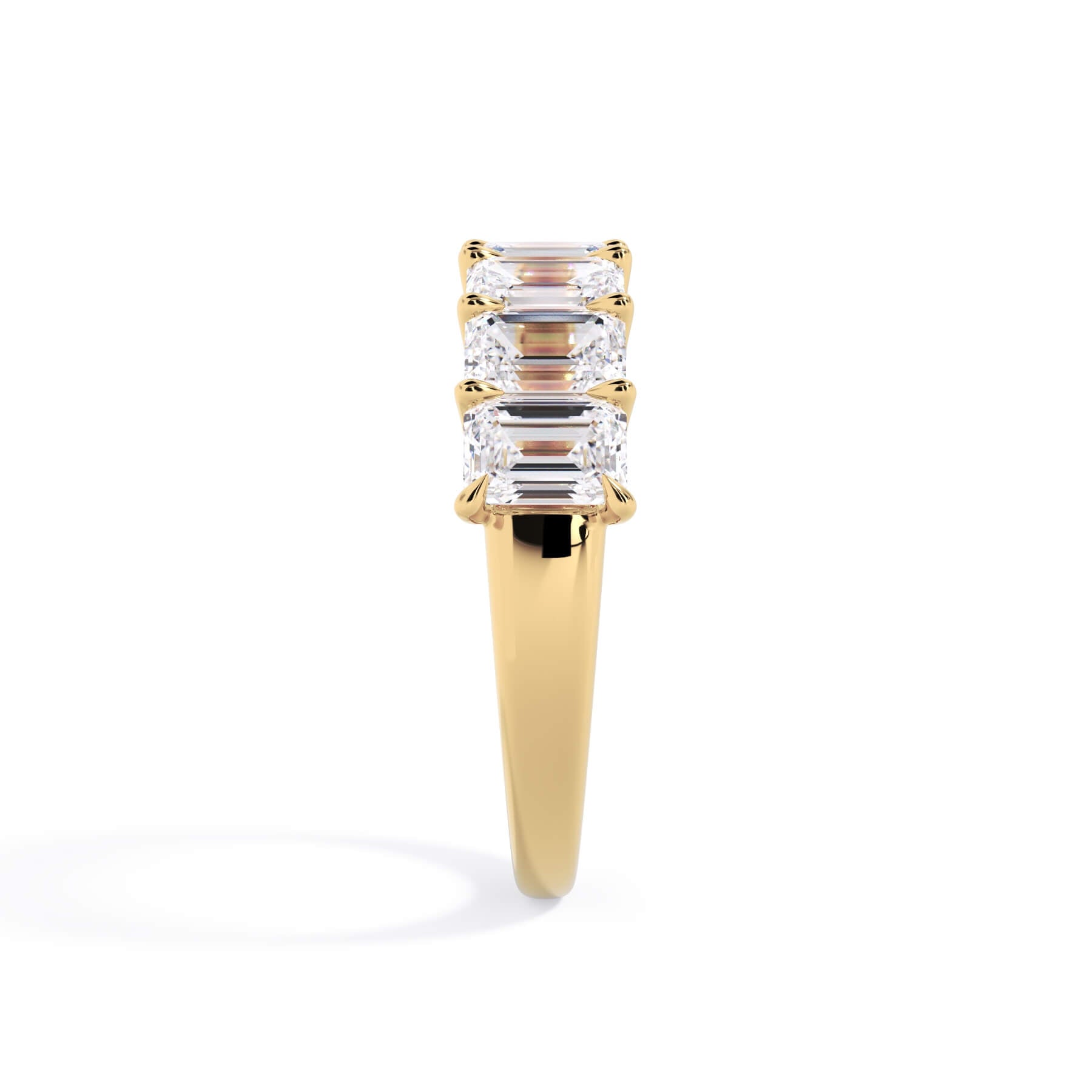 A picture of a seven stone diamond wedding ring with emerald cut diamonds that are U prong set in yellow gold on a white background with a side profile view.