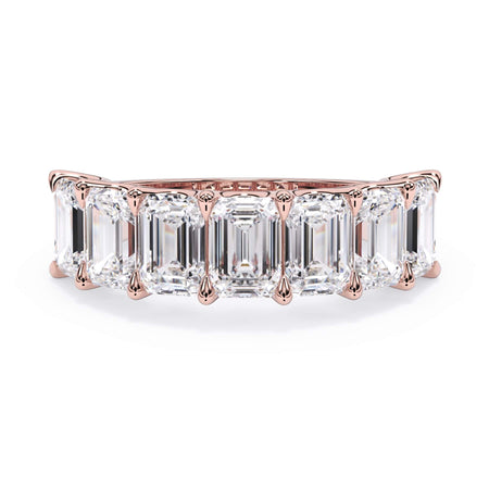 A picture of a seven stone diamond wedding ring with emerald cut diamonds that are U prong set in rose gold on a white background with the ring facing forward, lying down.
