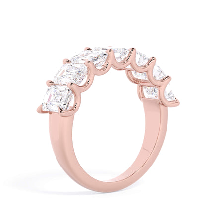 A picture of a seven stone diamond wedding ring with emerald cut diamonds that are U prong set in rose gold on a white background with a slightly angled, through the finger view.
