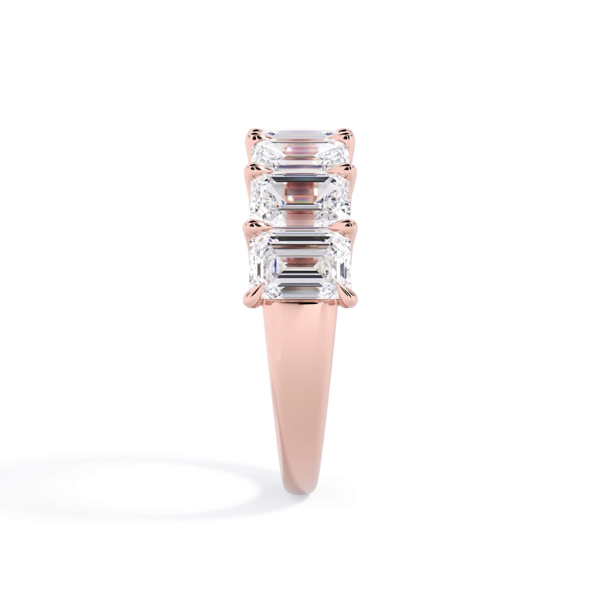 A picture of a seven stone diamond wedding ring with emerald cut diamonds that are U prong set in rose gold on a white background with a side profile view.