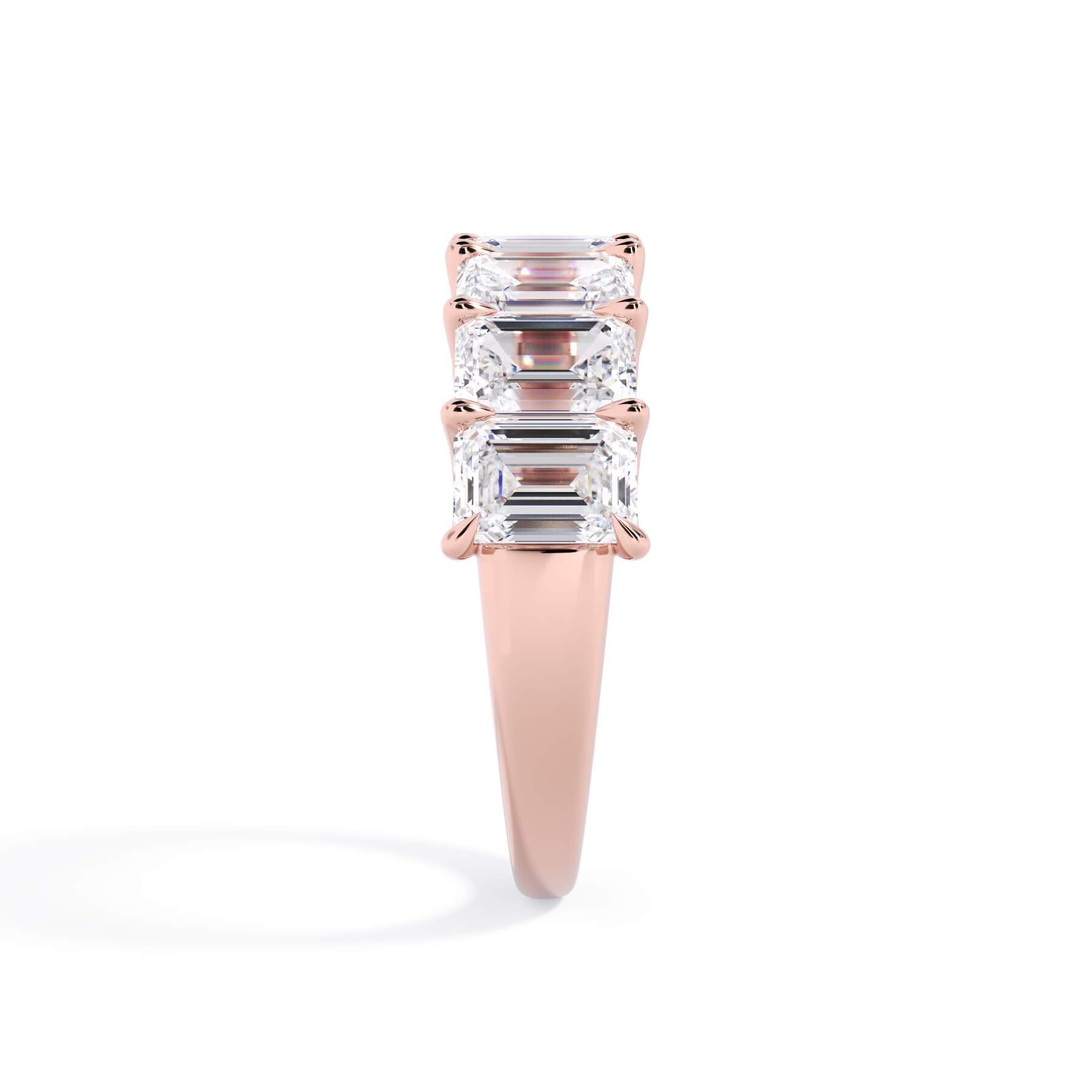 A picture of a seven stone diamond wedding ring with emerald cut diamonds that are U prong set in rose gold on a white background with a side profile view.