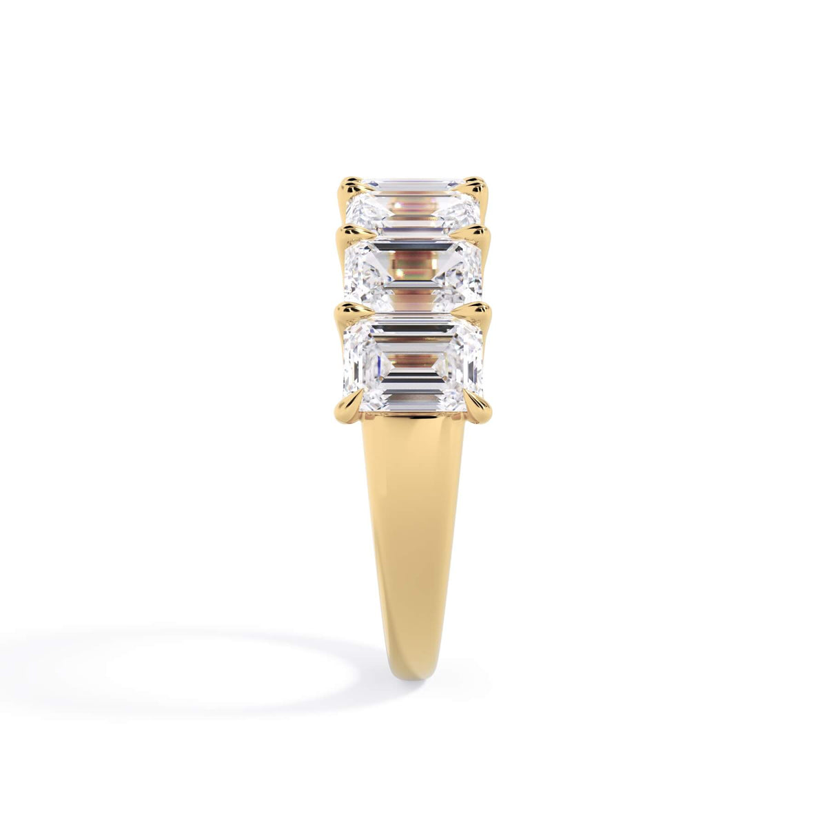 A picture of a seven stone diamond wedding ring with emerald cut diamonds that are U prong set in yellow gold on a white background with a side profile view.