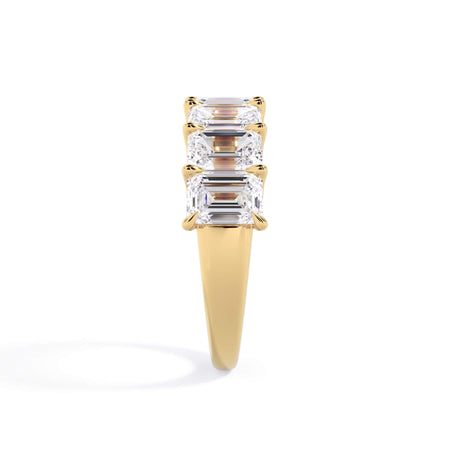 A picture of a seven stone diamond wedding ring with emerald cut diamonds that are U prong set in yellow gold on a white background with a side profile view.