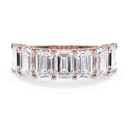 A picture of a seven stone diamond wedding ring with emerald cut diamonds that are U prong set in rose gold on a white background with the ring facing forward, lying down.
