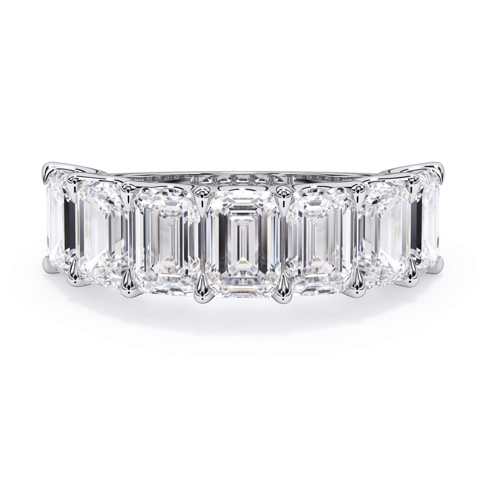 A picture of a seven stone diamond wedding ring with emerald cut diamonds that are U prong set in white gold or platinum on a white background with the ring facing forward, lying down.
