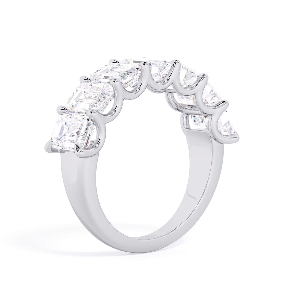 A picture of a seven stone diamond wedding ring with emerald cut diamonds that are U prong set in white gold or platinum on a white background with a slightly angled, through the finger view.