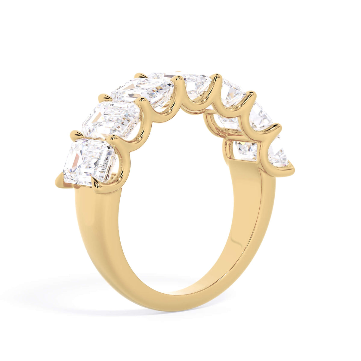 A picture of a seven stone diamond wedding ring with emerald cut diamonds that are U prong set in yellow gold on a white background with a slightly angled, through the finger view.