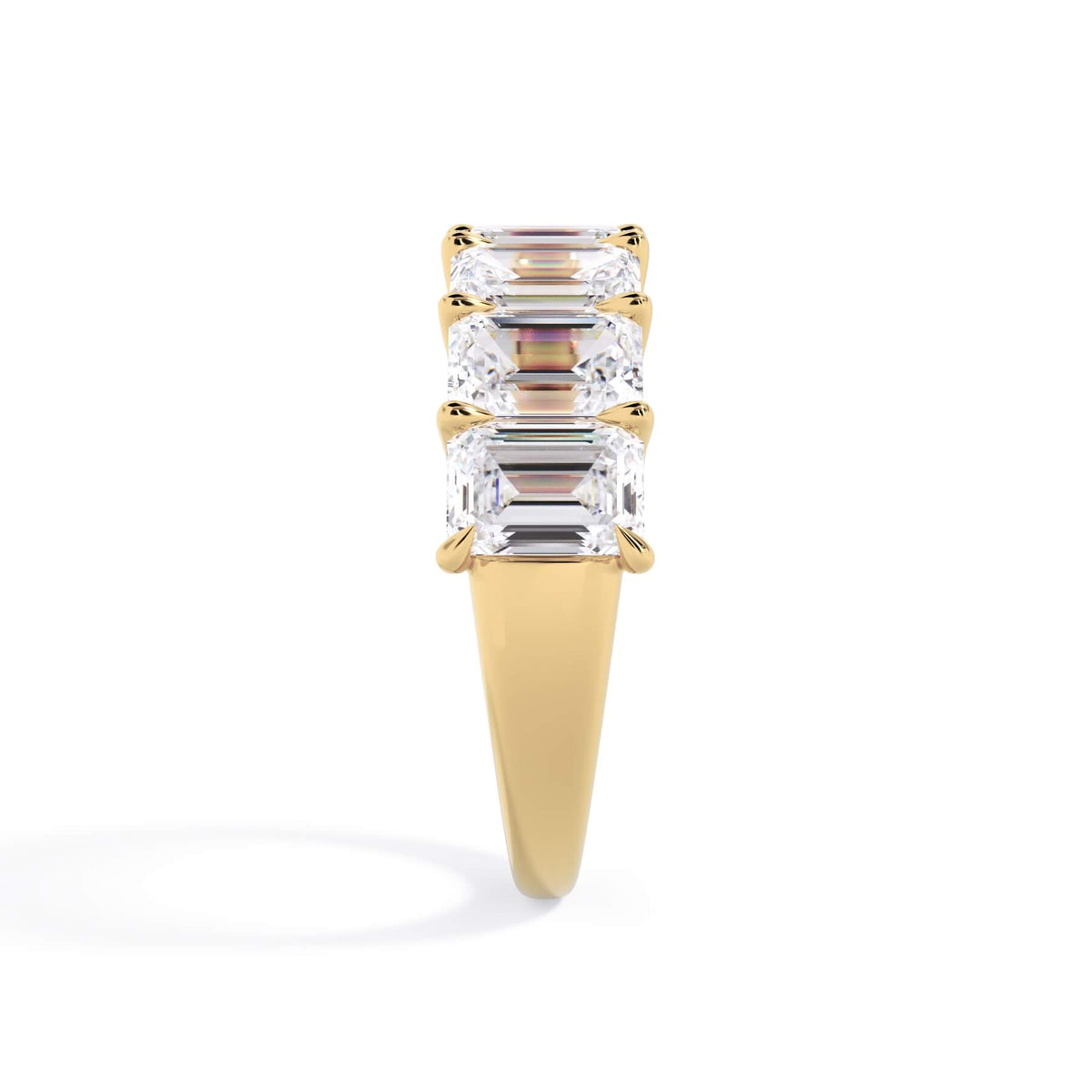 A picture of a seven stone diamond wedding ring with emerald cut diamonds that are U prong set in yellow gold on a white background with a side profile view.