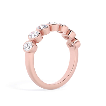 A picture of a seven stone diamond wedding ring with oval shaped diamonds that are bezel set in rose gold on a white background with a slightly angled, through the finger view.