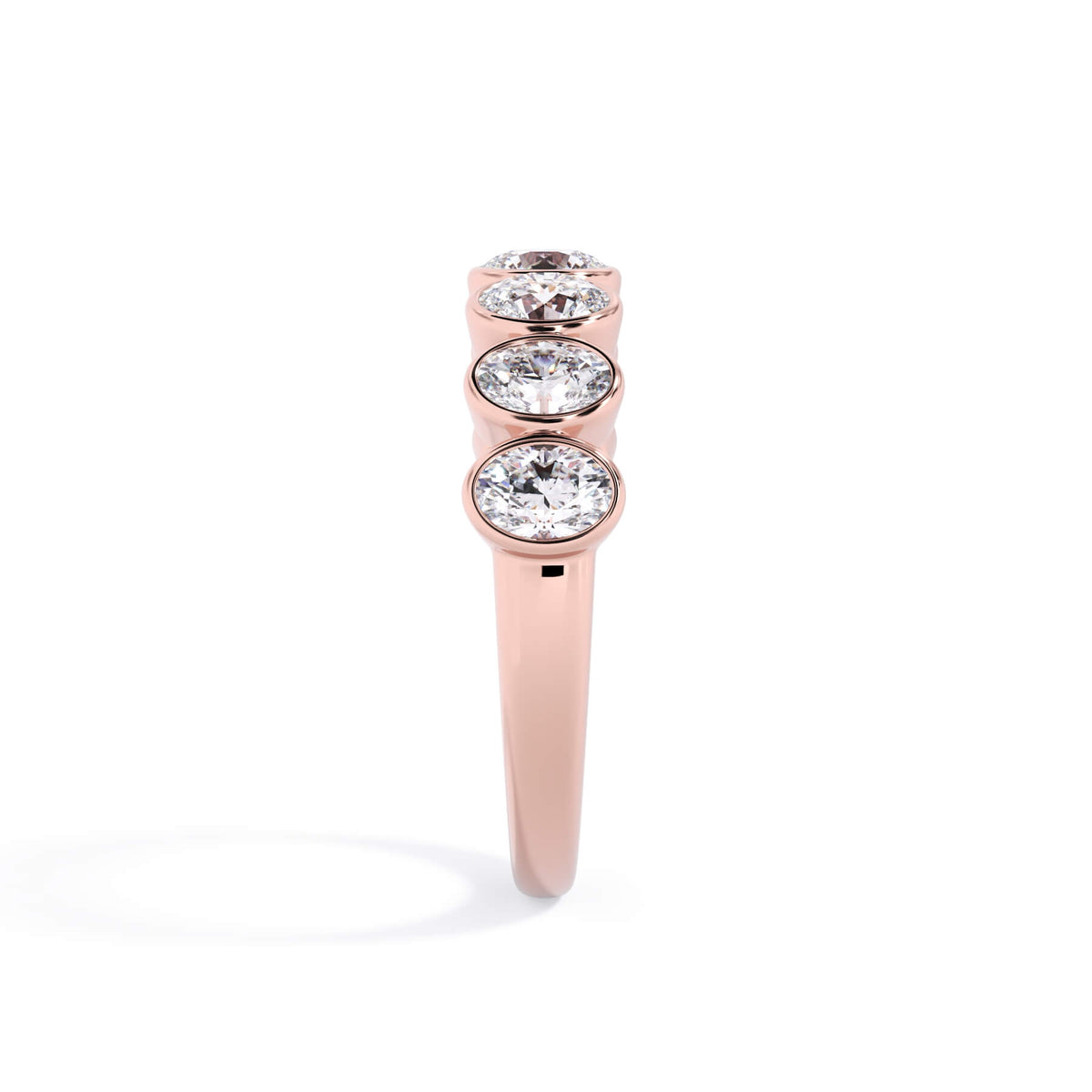 A picture of a seven stone diamond wedding ring with oval shaped diamonds that are bezel set in rose gold on a white background with a side profile view.