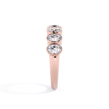 A picture of a seven stone diamond wedding ring with oval shaped diamonds that are bezel set in rose gold on a white background with a side profile view.