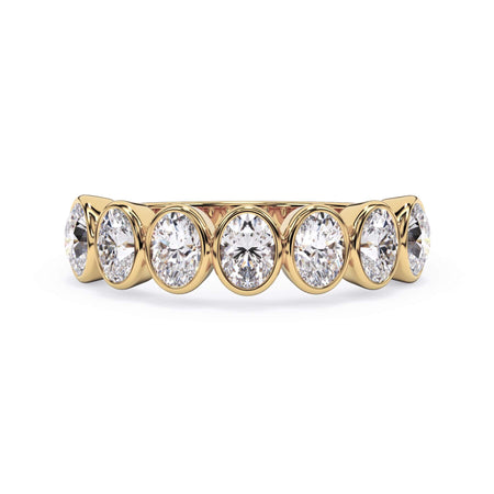 A picture of a seven stone diamond wedding ring with oval shaped diamonds that are bezel set in yellow gold on a white background with the ring facing forward, lying down.