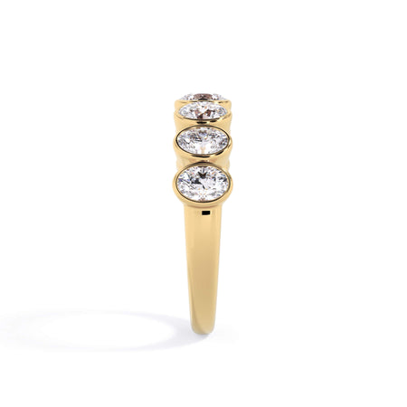 A picture of a seven stone diamond wedding ring with oval shaped diamonds that are bezel set in yellow gold on a white background with a side profile view.