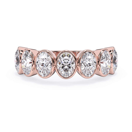 A picture of a seven stone diamond wedding ring with oval shaped diamonds that are bezel set in rose gold on a white background with the ring facing forward, lying down.