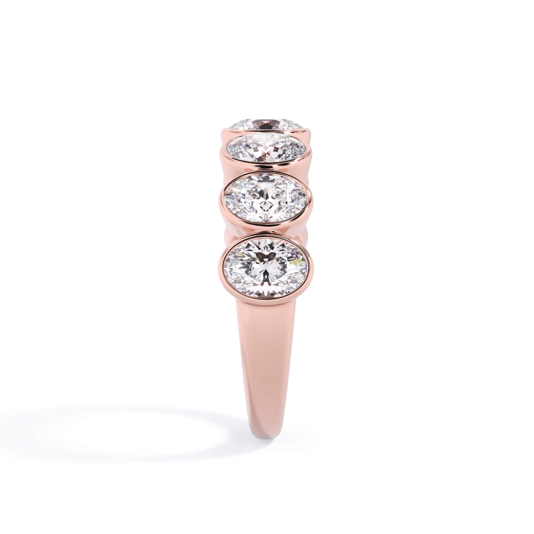 A picture of a seven stone diamond wedding ring with oval shaped diamonds that are bezel set in rose gold on a white background with a side profile view.