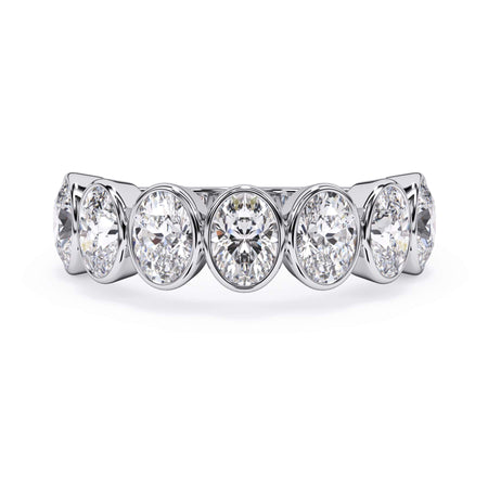 A picture of a seven stone diamond wedding ring with oval shaped diamonds that are bezel set in white gold or platinum on a white background with the ring facing forward, lying down.