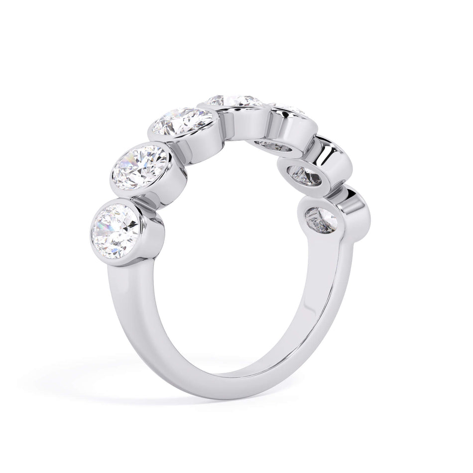 A picture of a seven stone diamond wedding ring with oval shaped diamonds that are bezel set in white gold or platinum on a white background with a slightly angled, through the finger view.