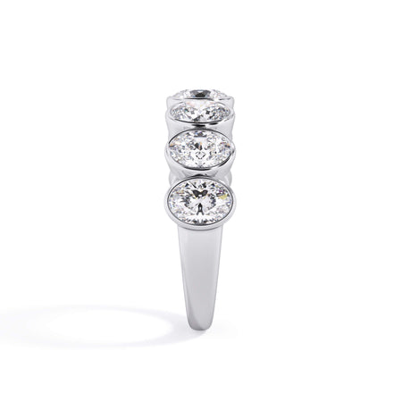 A picture of a seven stone diamond wedding ring with oval shaped diamonds that are bezel set in white gold or platinum on a white background with a side profile view.