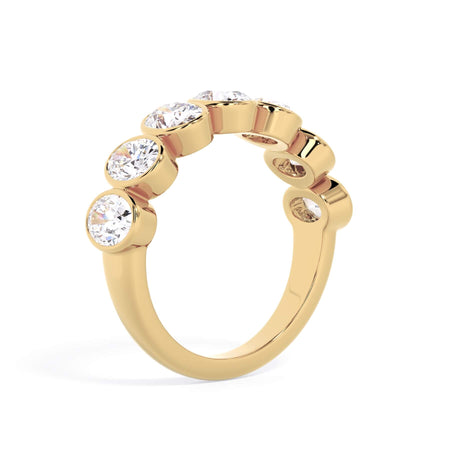 A picture of a seven stone diamond wedding ring with oval shaped diamonds that are bezel set in yellow gold on a white background with a slightly angled, through the finger view.