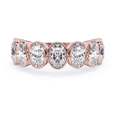 A picture of a seven stone diamond wedding ring with oval shaped diamonds that are bezel set in rose gold on a white background with the ring facing forward, lying down.