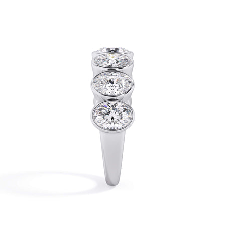 A picture of a seven stone diamond wedding ring with oval shaped diamonds that are bezel set in white gold or platinum on a white background with a side profile view.