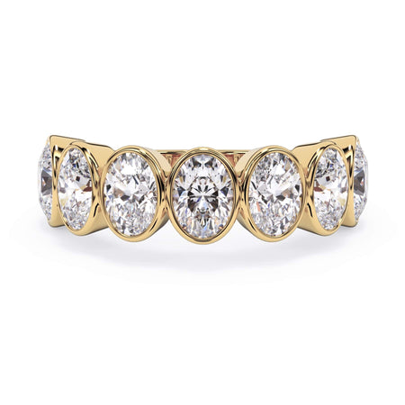 A picture of a seven stone diamond wedding ring with oval shaped diamonds that are bezel set in yellow gold on a white background with the ring facing forward, lying down.