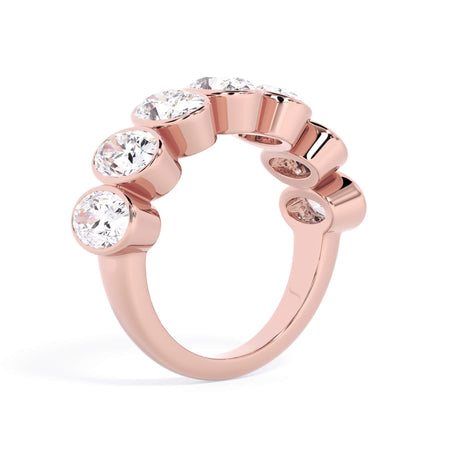 A picture of a seven stone diamond wedding ring with oval shaped diamonds that are bezel set in rose gold on a white background with a slightly angled, through the finger view.