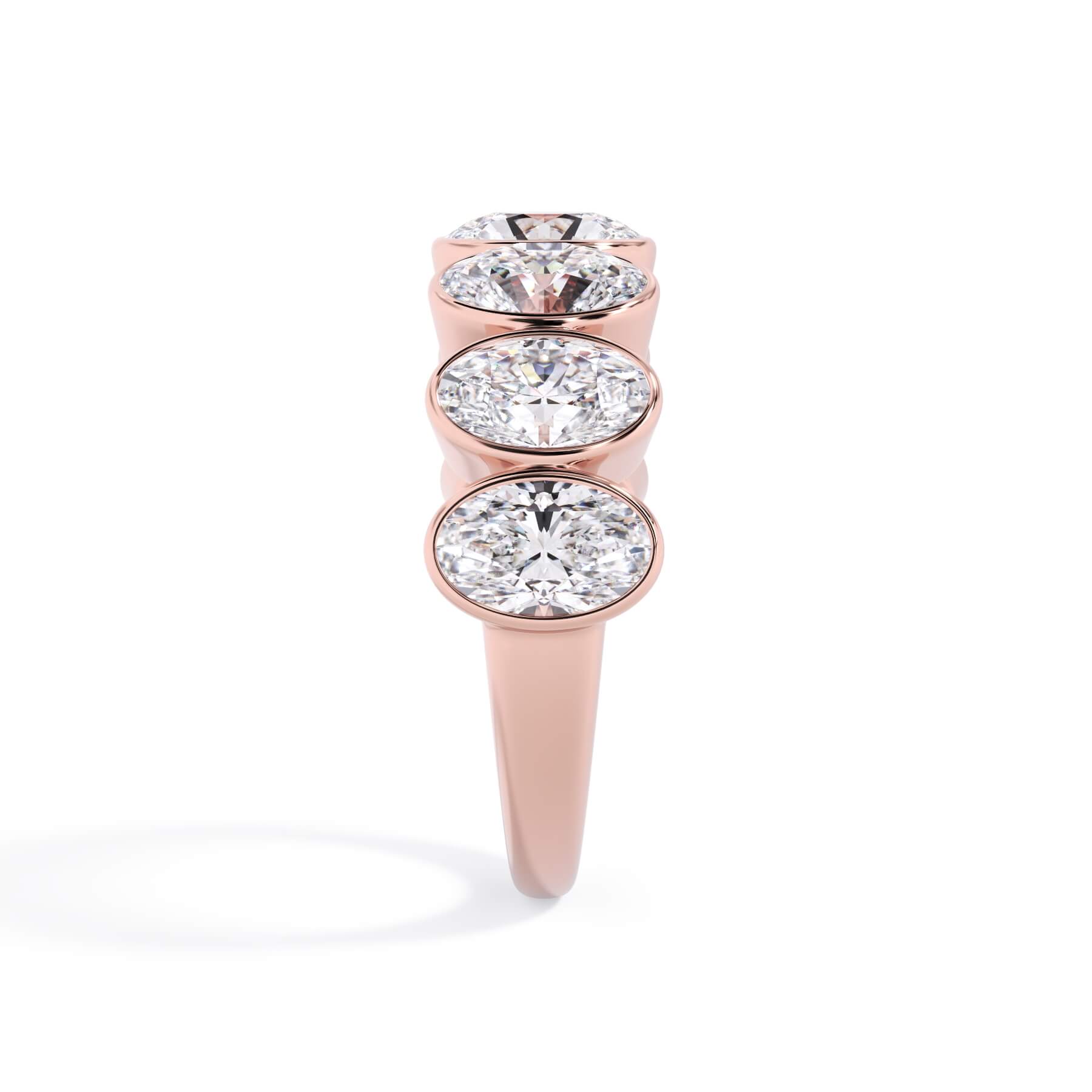 A picture of a seven stone diamond wedding ring with oval shaped diamonds that are bezel set in rose gold on a white background with a side profile view.