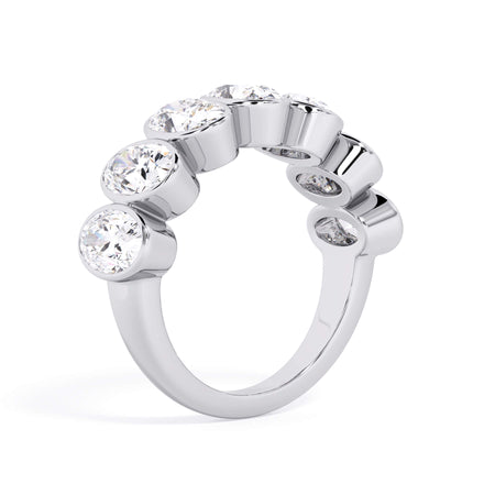 A picture of a seven stone diamond wedding ring with oval shaped diamonds that are bezel set in white gold or platinum on a white background with a slightly angled, through the finger view.