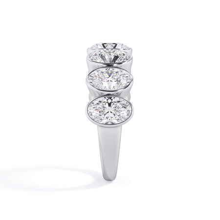 A picture of a seven stone diamond wedding ring with oval shaped diamonds that are bezel set in white gold or platinum on a white background with a side profile view.