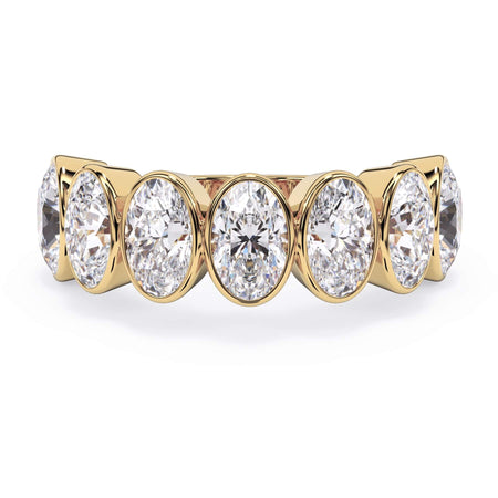 A picture of a seven stone diamond wedding ring with oval shaped diamonds that are bezel set in yellow gold on a white background with the ring facing forward, lying down.