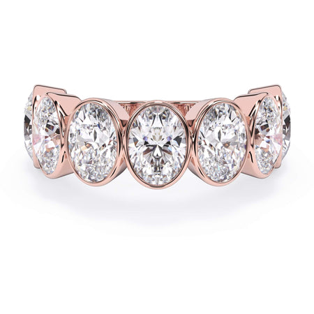 A picture of a seven stone diamond wedding ring with oval shaped diamonds that are bezel set in rose gold on a white background with the ring facing forward, lying down.