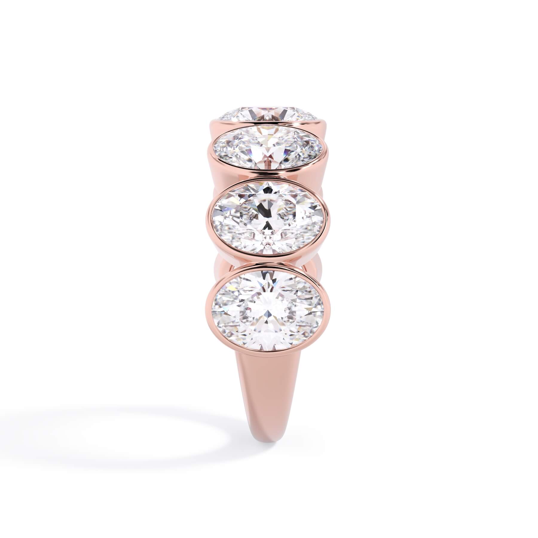 A picture of a seven stone diamond wedding ring with oval shaped diamonds that are bezel set in rose gold on a white background with a side profile view.