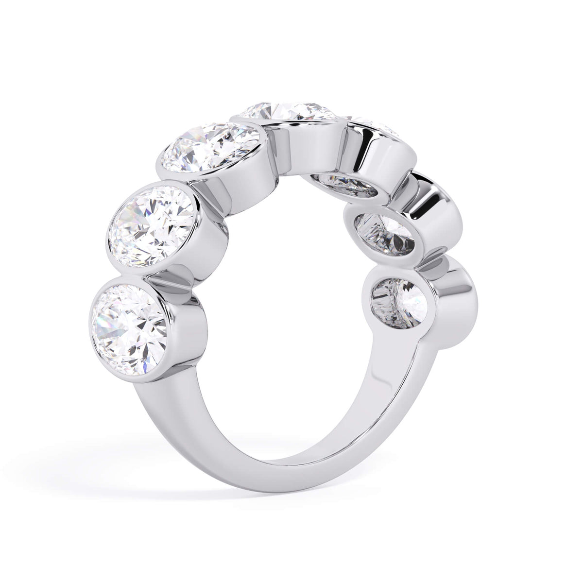 A picture of a seven stone diamond wedding ring with oval shaped diamonds that are bezel set in white gold or platinum on a white background with a slightly angled, through the finger view.
