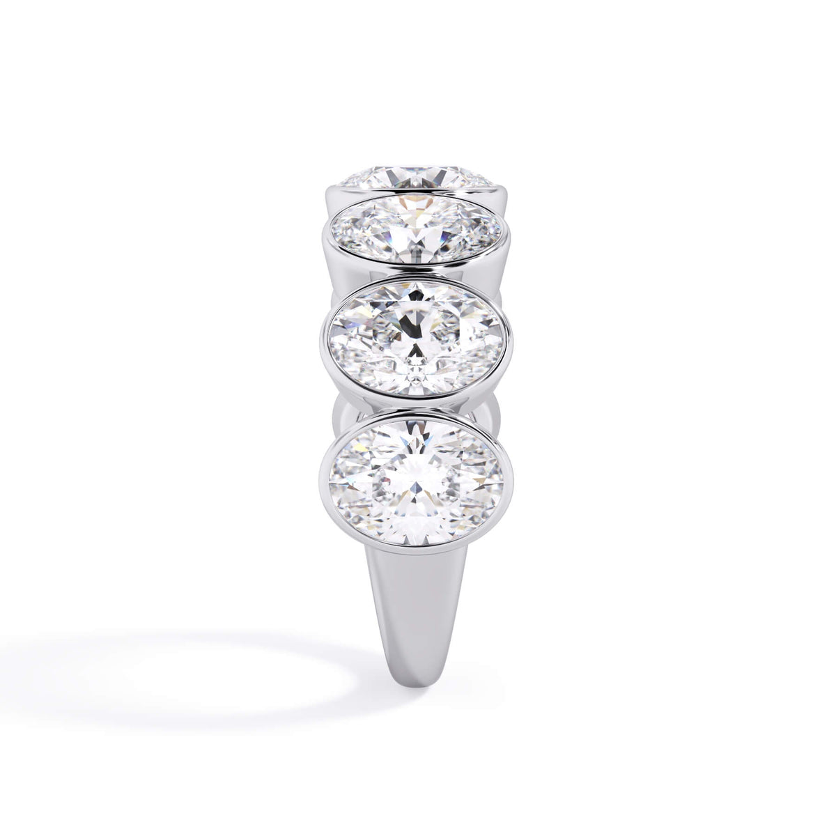 A picture of a seven stone diamond wedding ring with oval shaped diamonds that are bezel set in white gold or platinum on a white background with a side profile view.