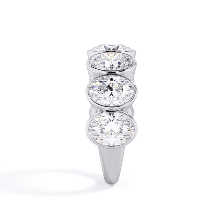 A picture of a seven stone diamond wedding ring with oval shaped diamonds that are bezel set in white gold or platinum on a white background with a side profile view.
