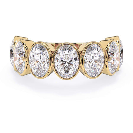 A picture of a seven stone diamond wedding ring with oval shaped diamonds that are bezel set in yellow gold on a white background with the ring facing forward, lying down.