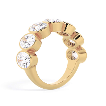 A picture of a seven stone diamond wedding ring with oval shaped diamonds that are bezel set in yellow gold on a white background with a slightly angled, through the finger view.