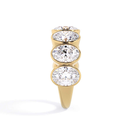 A picture of a seven stone diamond wedding ring with oval shaped diamonds that are bezel set in yellow gold on a white background with a side profile view.