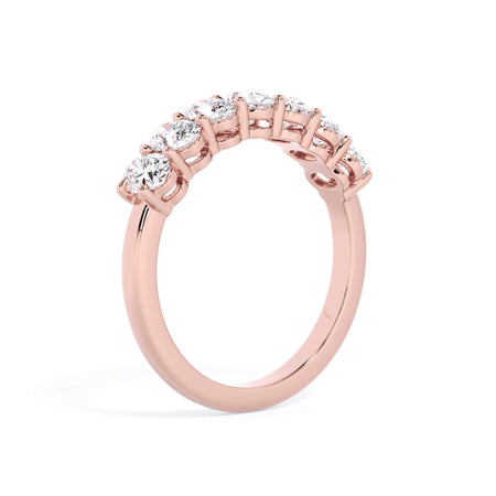 A picture of a seven stone diamond wedding ring with oval shaped diamonds that are shared prong set in rose gold on a white background with a slightly angled, through the finger view.