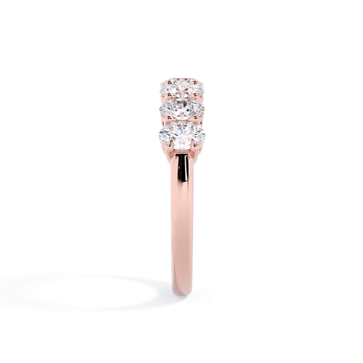 A picture of a seven stone diamond wedding ring with oval shaped diamonds that are shared prong set in rose gold on a white background with a side profile view.
